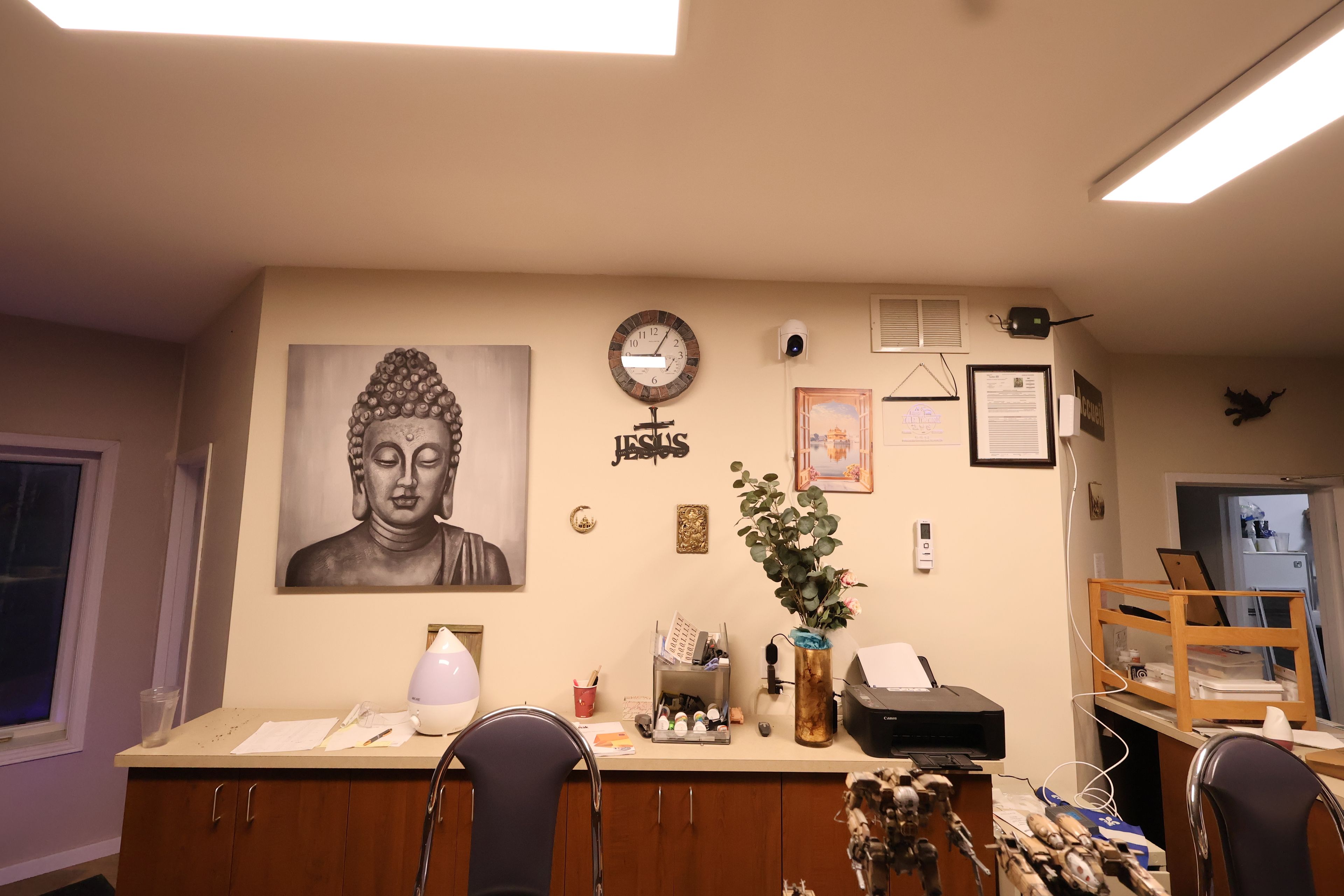 Een kamer met een Boeddha-schilderij, een klok, een beveiligingscamera en een bureau met een printer.