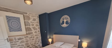 Quarto com cama, duas luminárias de cabeceira, tapeçaria na parede e um recorte decorativo de árvore.