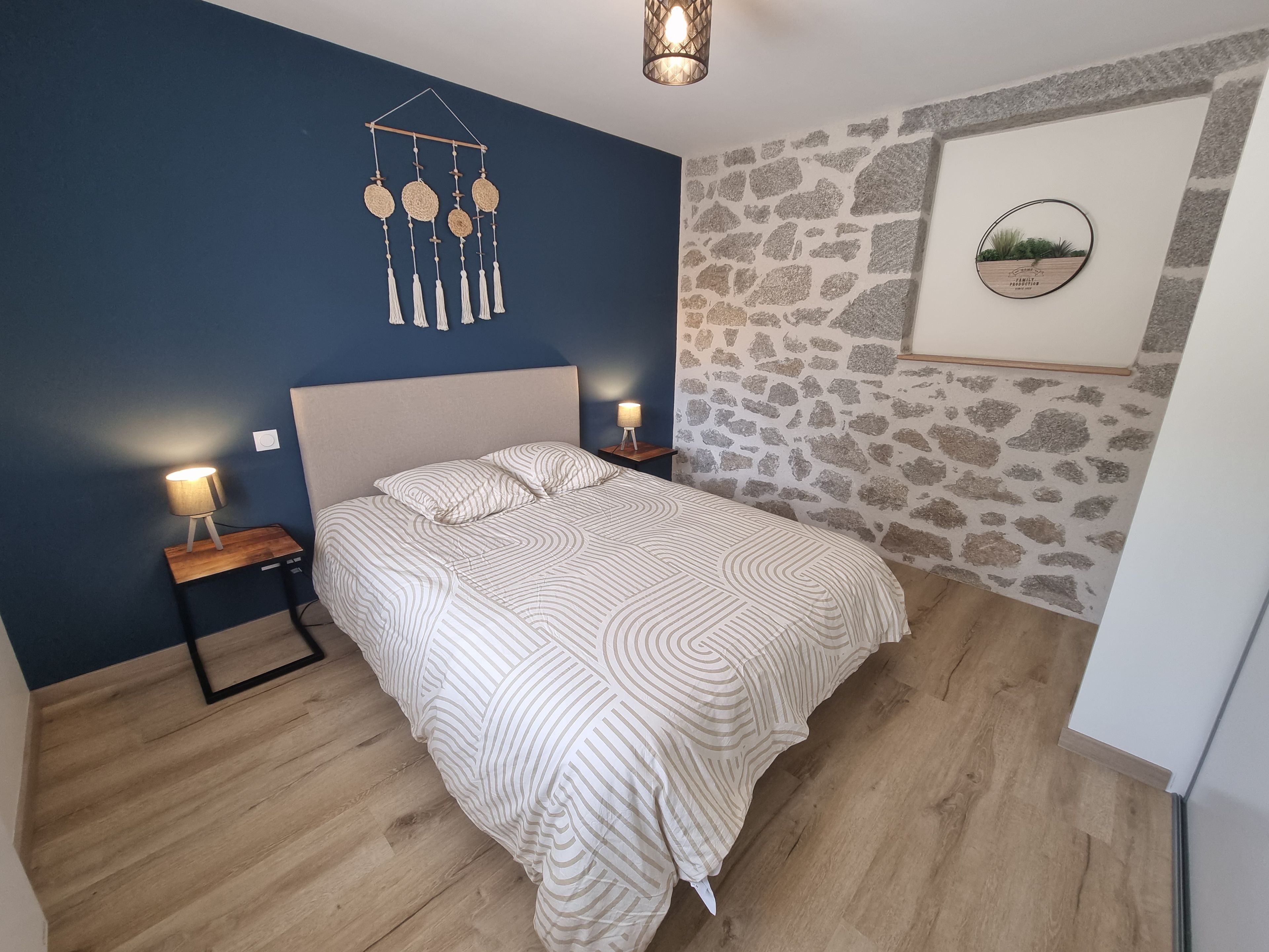 Un dormitorio con cama, lámparas de noche, una lámpara colgante en la pared y un revestimiento de pared con diseño de piedra.