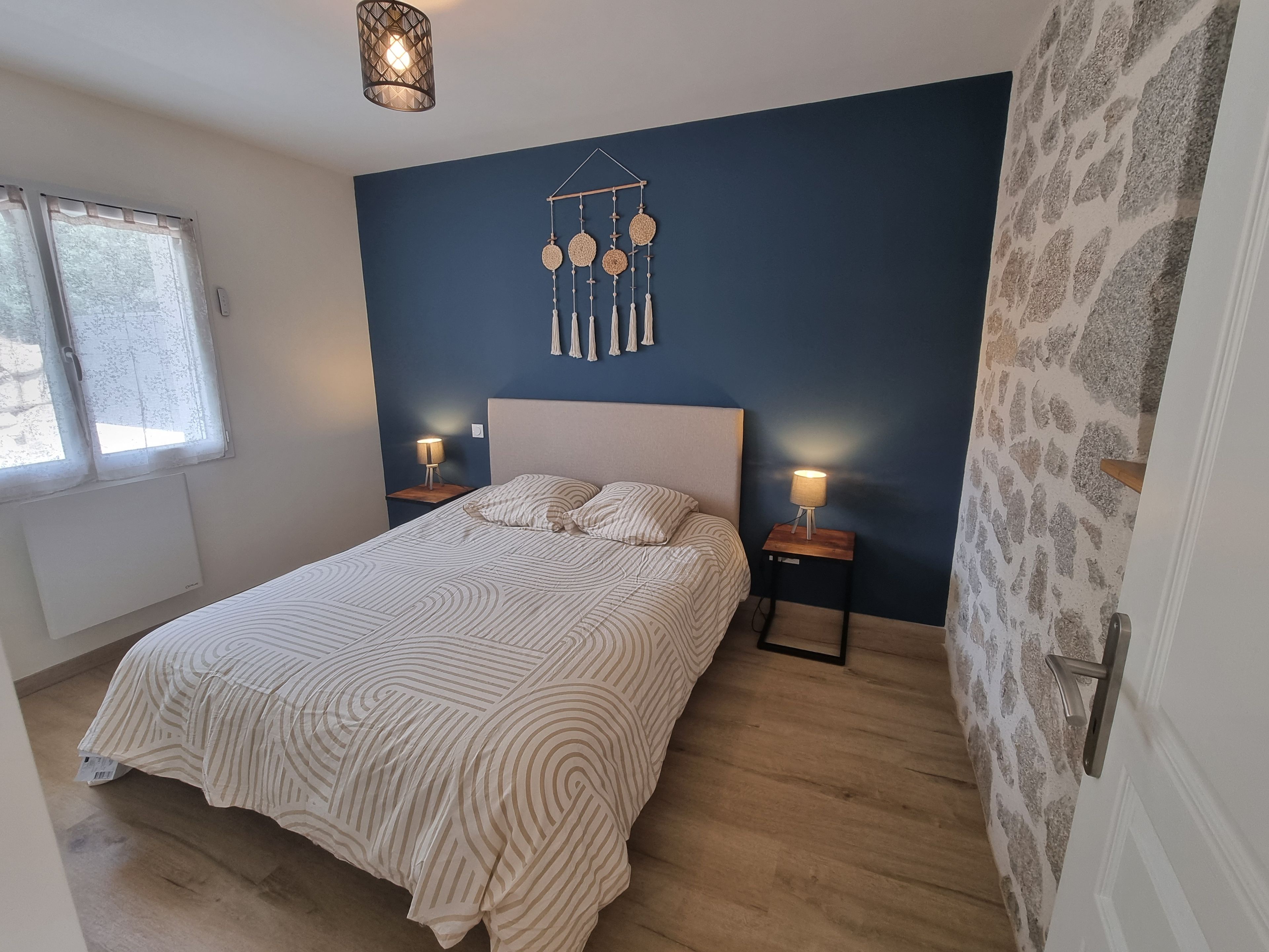 Quarto com uma cama, duas mesas de cabeceira, um objeto pendurado na parede e uma janela.
