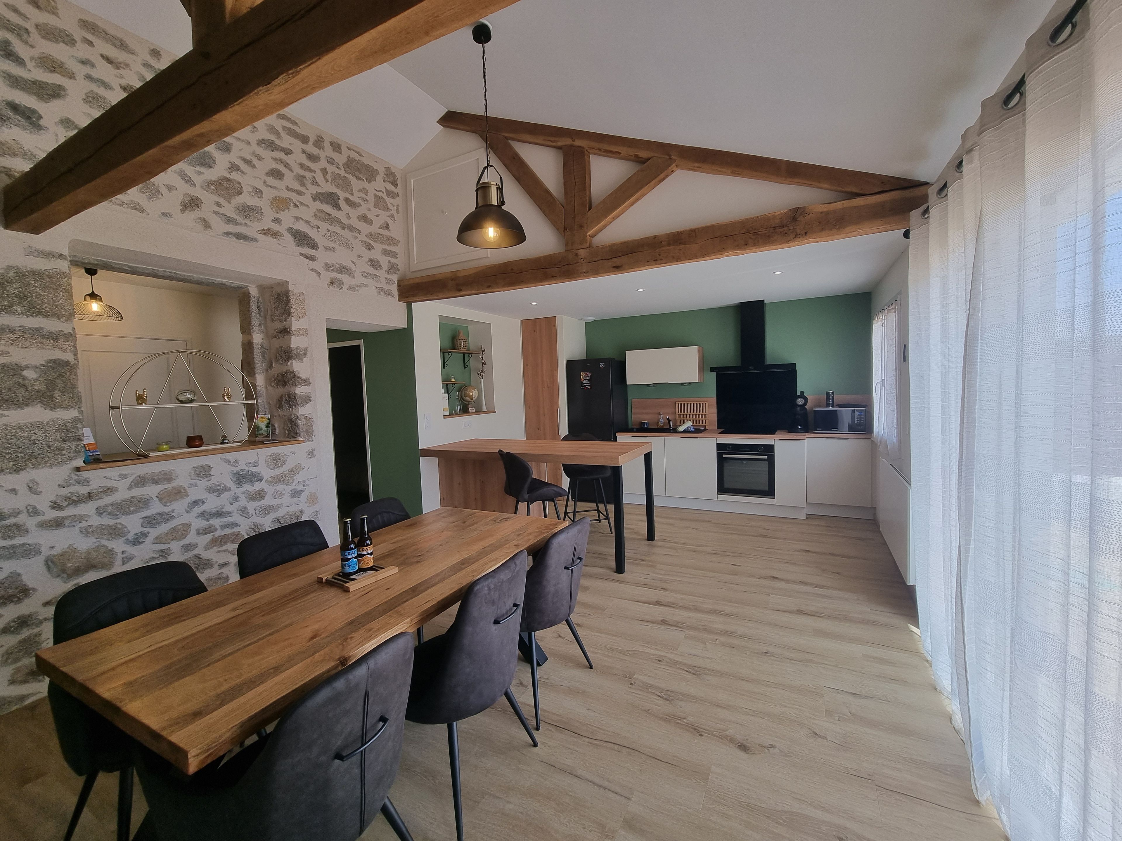 Una cocina moderna con horno empotrado, un comedor con mesa y sillas de madera, y una pared de piedra.