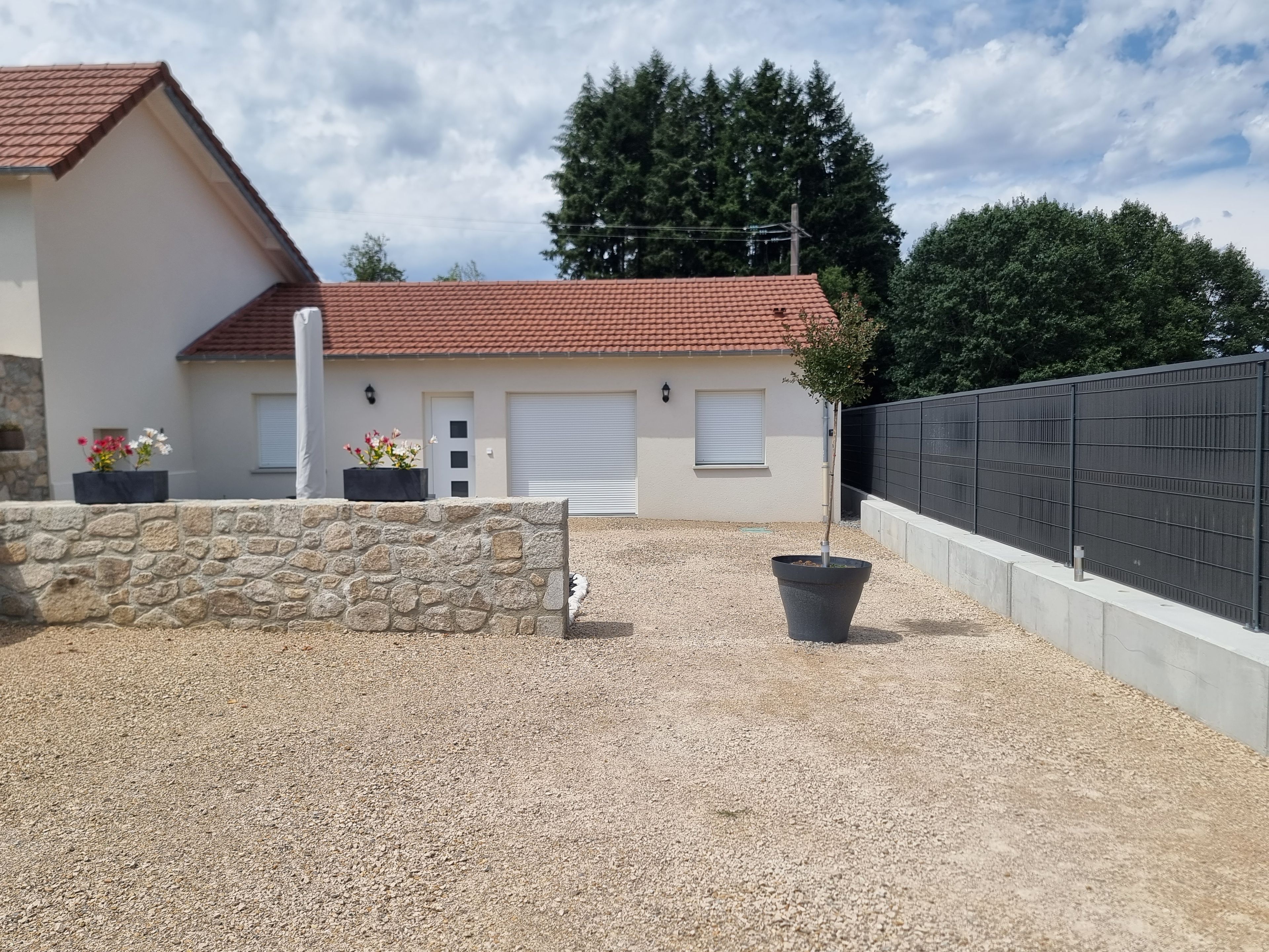 Il s’agit d’une propriété résidentielle dotée d’un mur en pierre, d’une allée en gravier, d’un toit recouvert de tuiles rouges et d’une clôture noire.