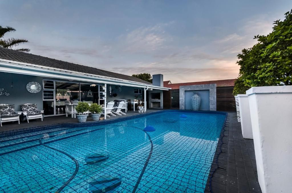 A swimming pool with a tiled deck, lounge chairs, and a covered seating area with tables and chairs.