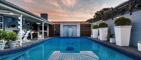 A swimming pool with a tiled floor, surrounded by potted plants and a covered seating area.
