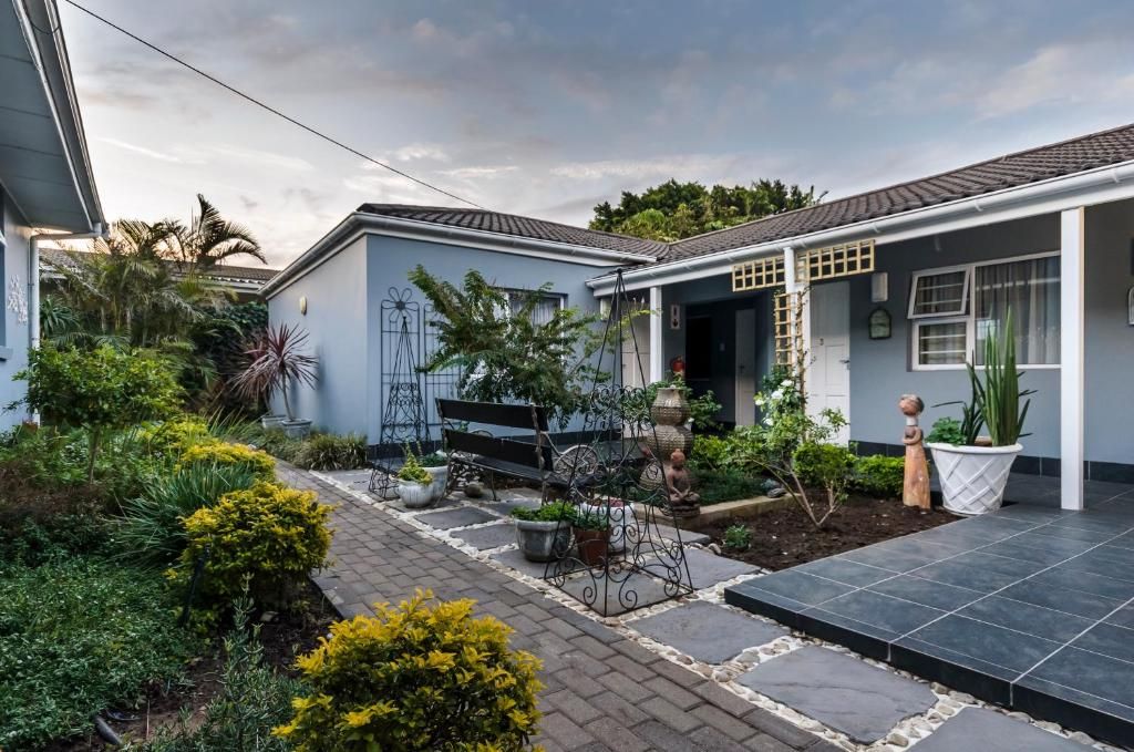 A residential property with a paved driveway, a garden with various plants, a bench, and a small statue.