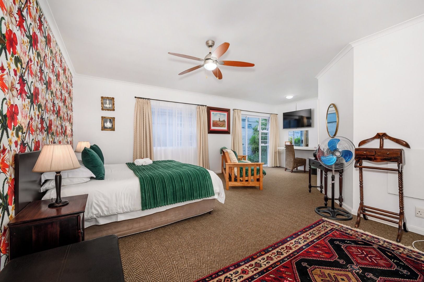 A hotel room with a bed, a desk, a chair, a fan, and a television.