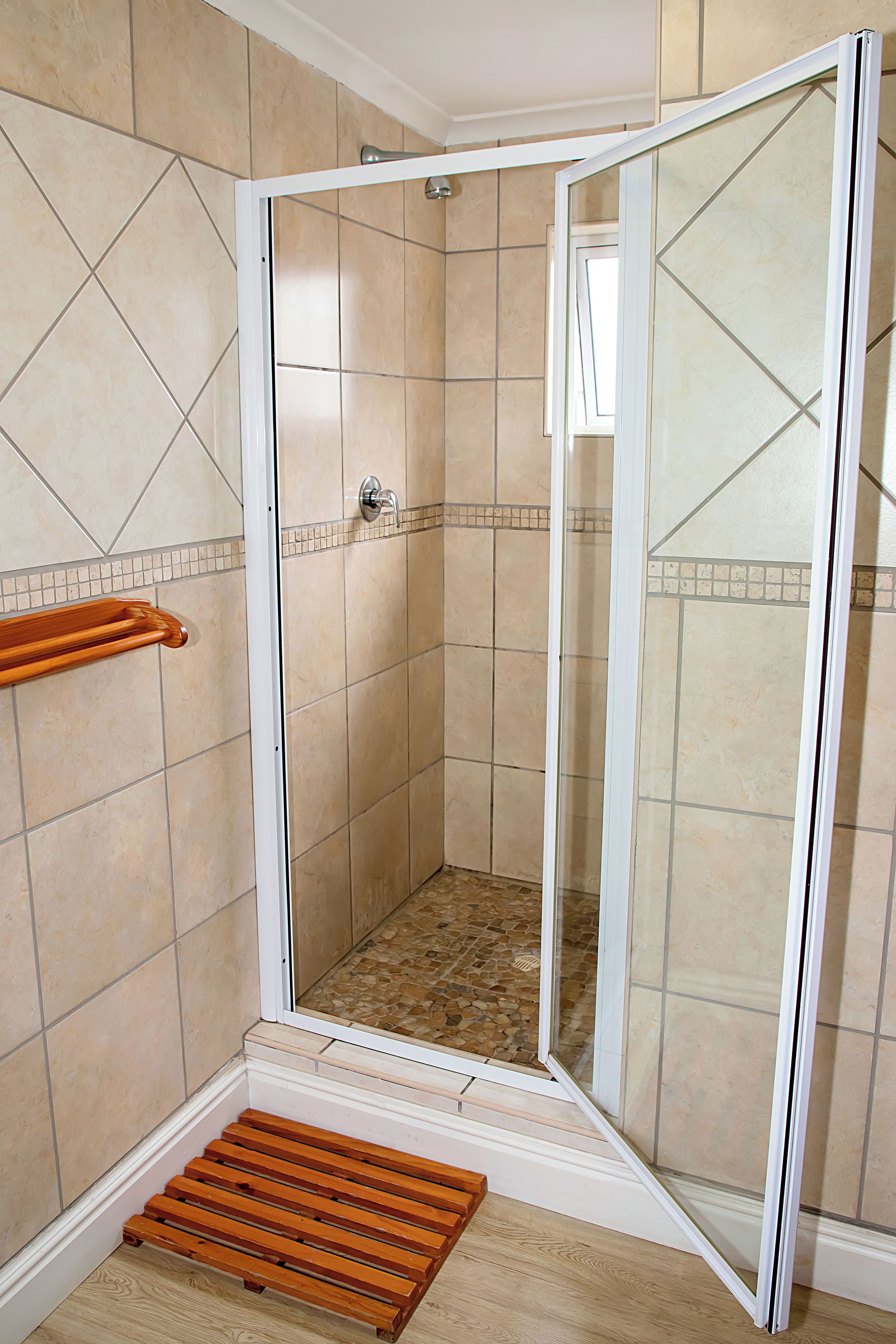 Un área de ducha con puerta de vidrio, un banco de madera y piso de baldosas.