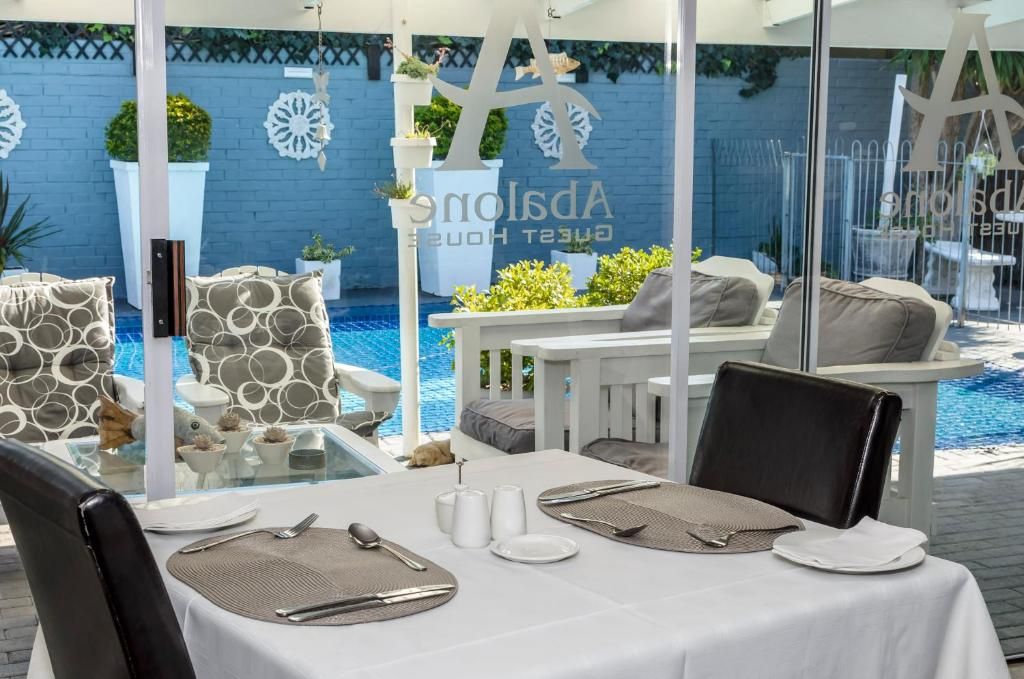 Comedor con mesa lista para dos personas, con vista a una piscina con pared azul y plantas decorativas.