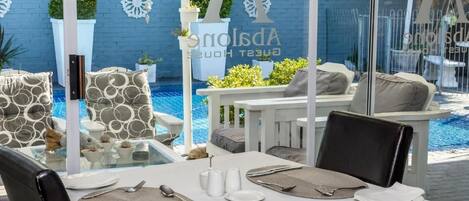 Comedor con mesa lista para dos personas, con vista a una piscina con pared azul y plantas decorativas.