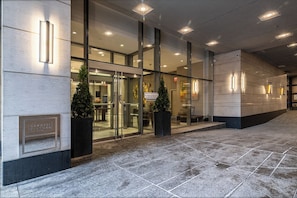 A modern hotel entrance with glass doors, a reception desk, and a sign indicating guest services.