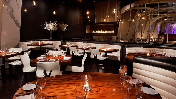 A restaurant interior with round tables, white chairs, and a central fireplace.