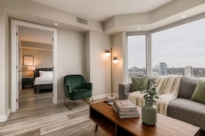 A modern living room with a large window, a green armchair, a wooden coffee table, and a sofa with a view of the city.