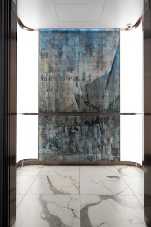 A modern elevator interior with a large abstract artwork on the walls and marble flooring.