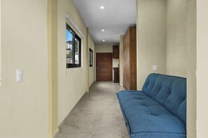 Un couloir avec un canapé bleu, une porte en bois et une fenêtre avec des stores.