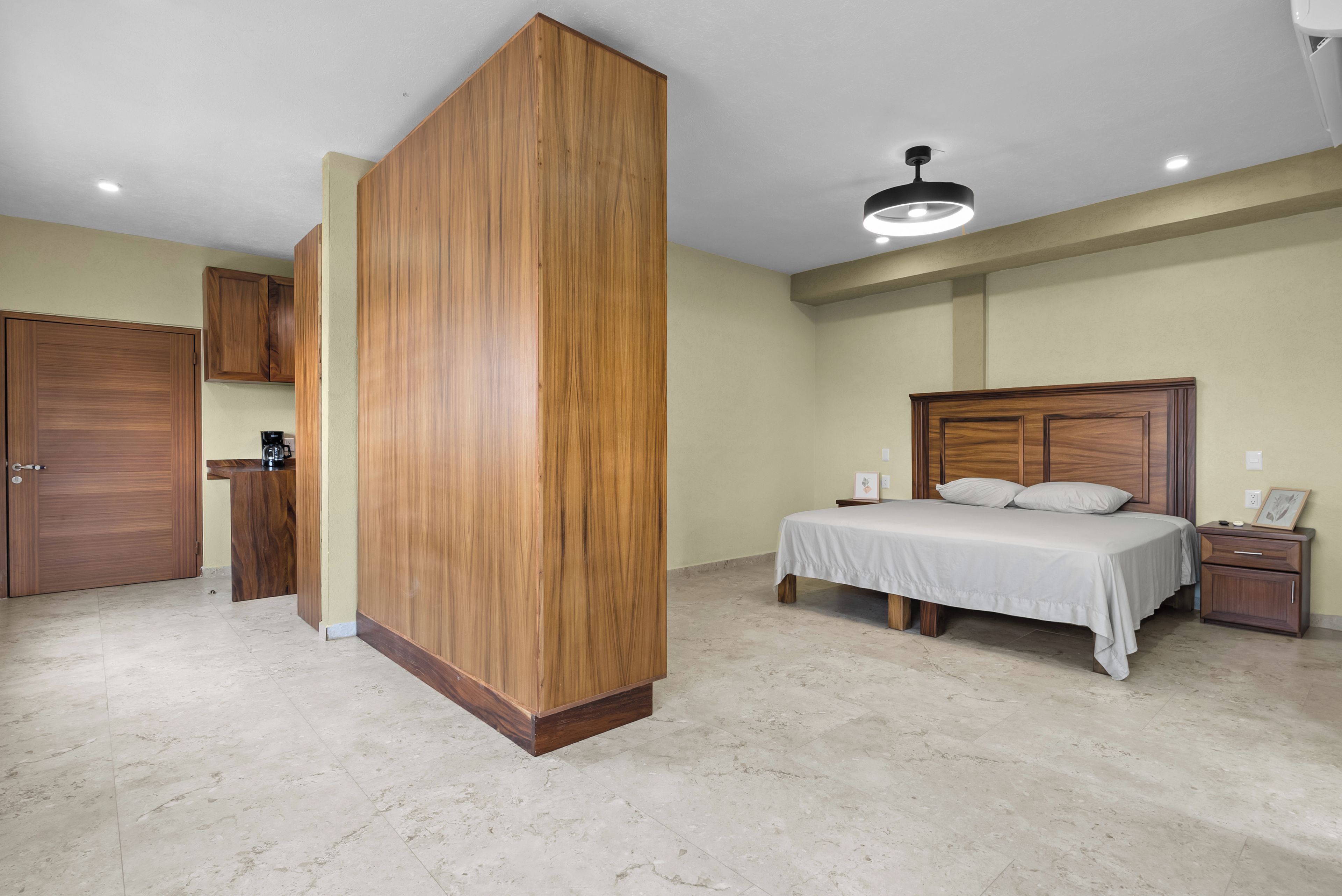 Un dormitorio con un armario de madera, una cama con ropa de cama blanca, una mesita de noche y una lámpara en el techo.