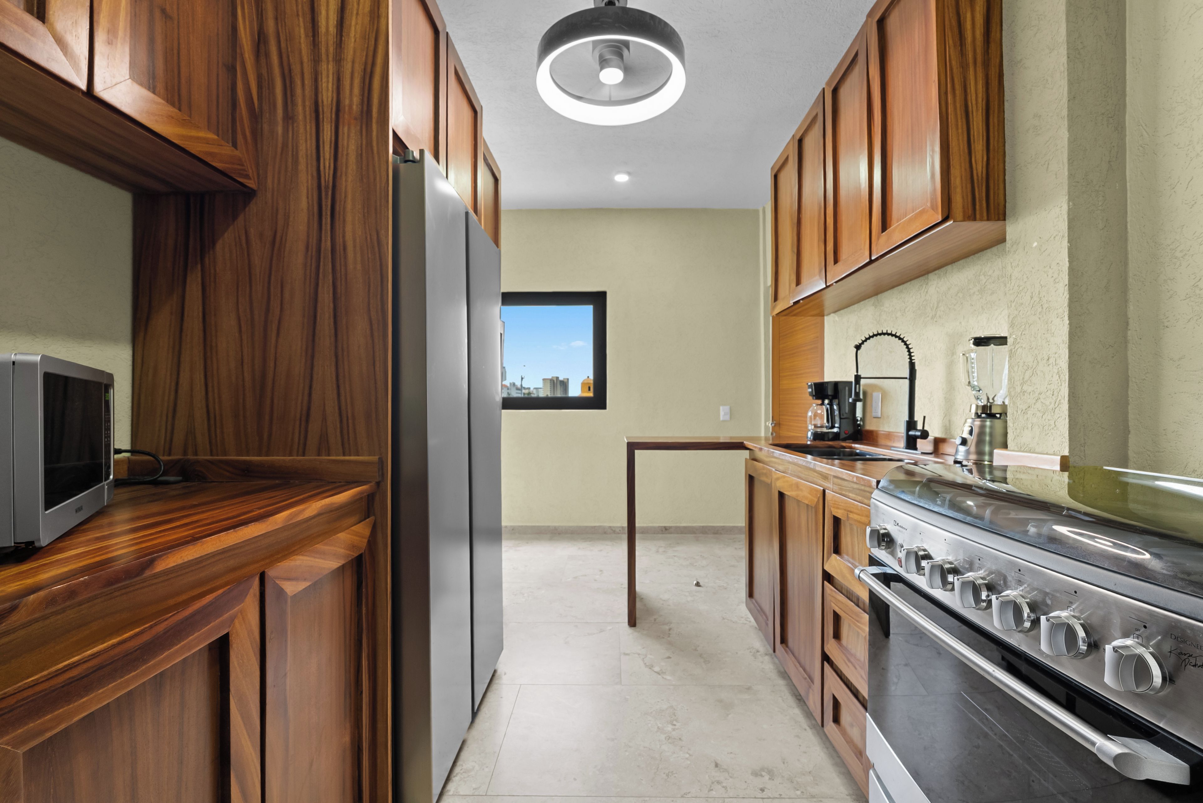 A modern kitchen with wooden cabinets, a stainless steel refrigerator, a stove, and a window with a city view.