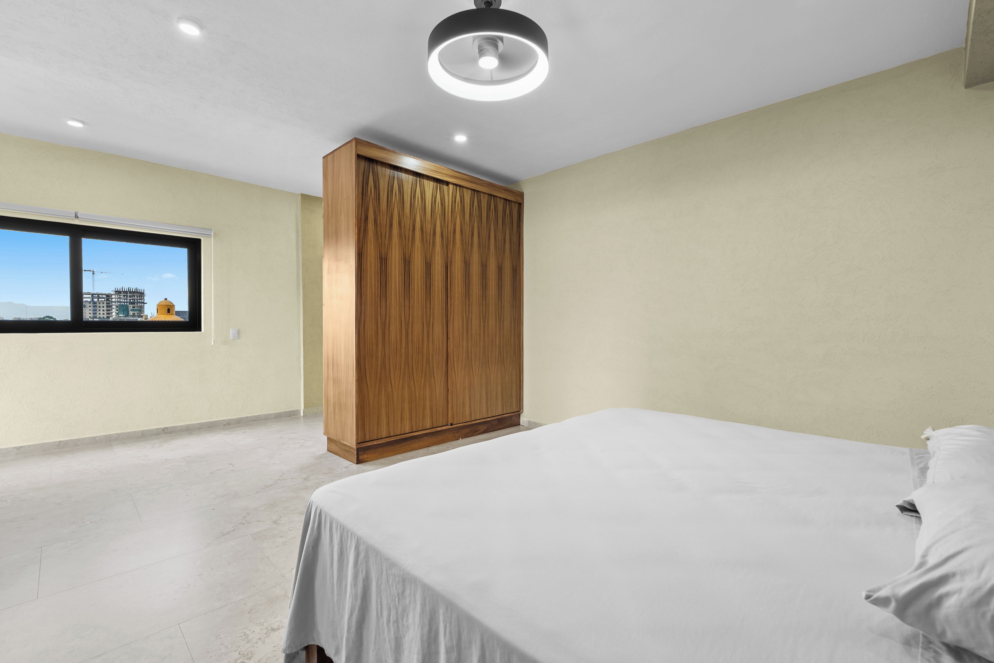 A bedroom with a bed, a wardrobe, a window, and a ceiling light.