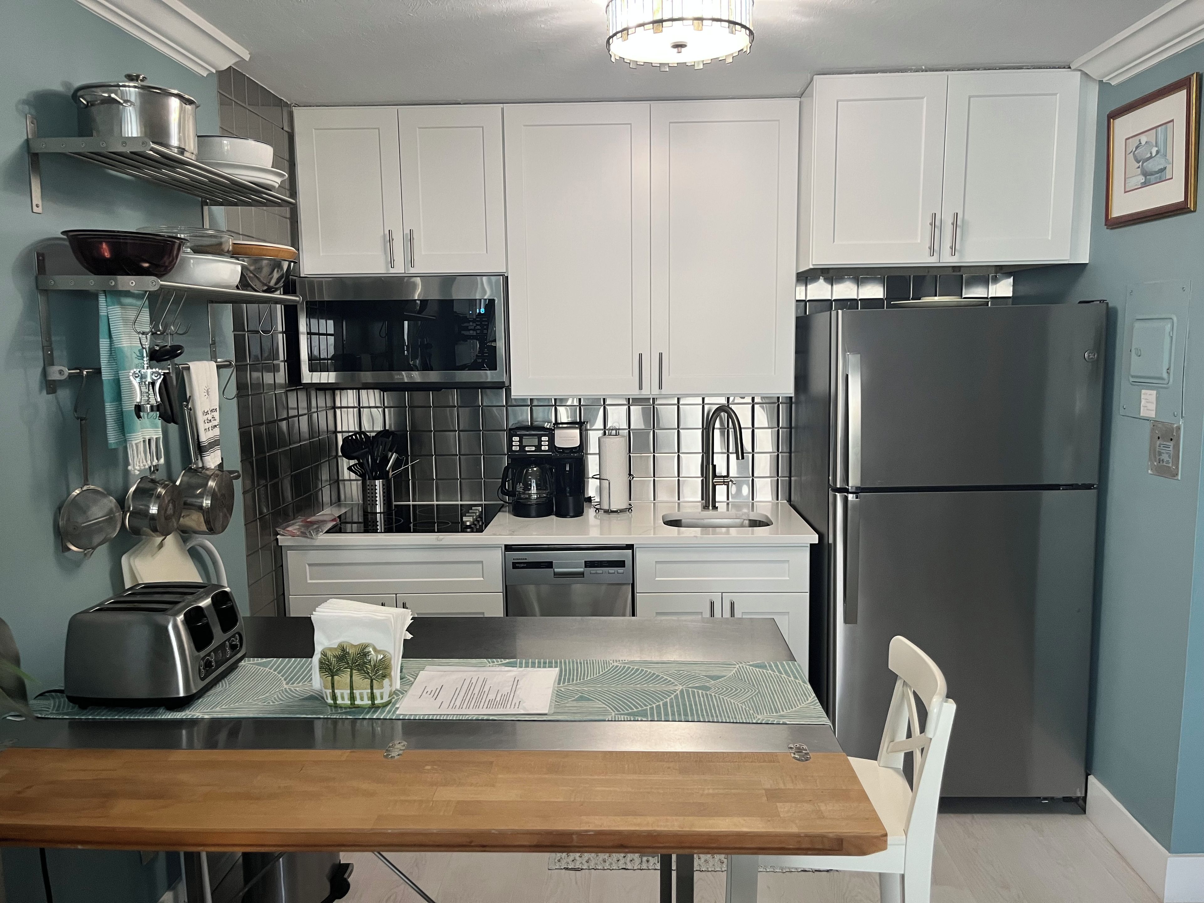A modern kitchen with white cabinets, stainless steel appliances, and a wooden dining table.