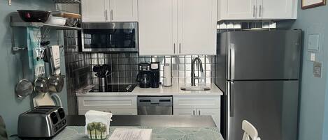 A modern kitchen with white cabinets, stainless steel appliances, and a wooden dining table.
