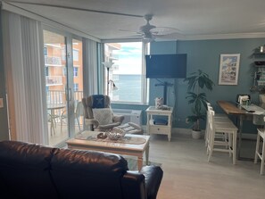 A living room with a leather sofa, a dining table with chairs, a TV, and a view of the ocean. - Breathtaking Gulf View from the 11th Floor in FMB (Fort Myers Beach)