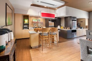 A modern kitchen with a dining area, wooden chairs, a bar counter, and a refrigerator. - TownePlace Suites Fort Worth SW/TCU 1BR Suite (Fort Worth)