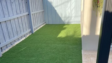 A backyard with artificial green grass, a white fence, and a decorative wall-mounted planter.