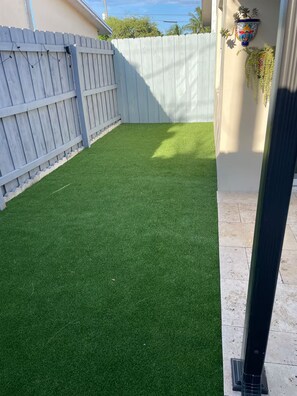 A backyard with artificial green grass, a white fence, and a decorative wall-mounted planter.
