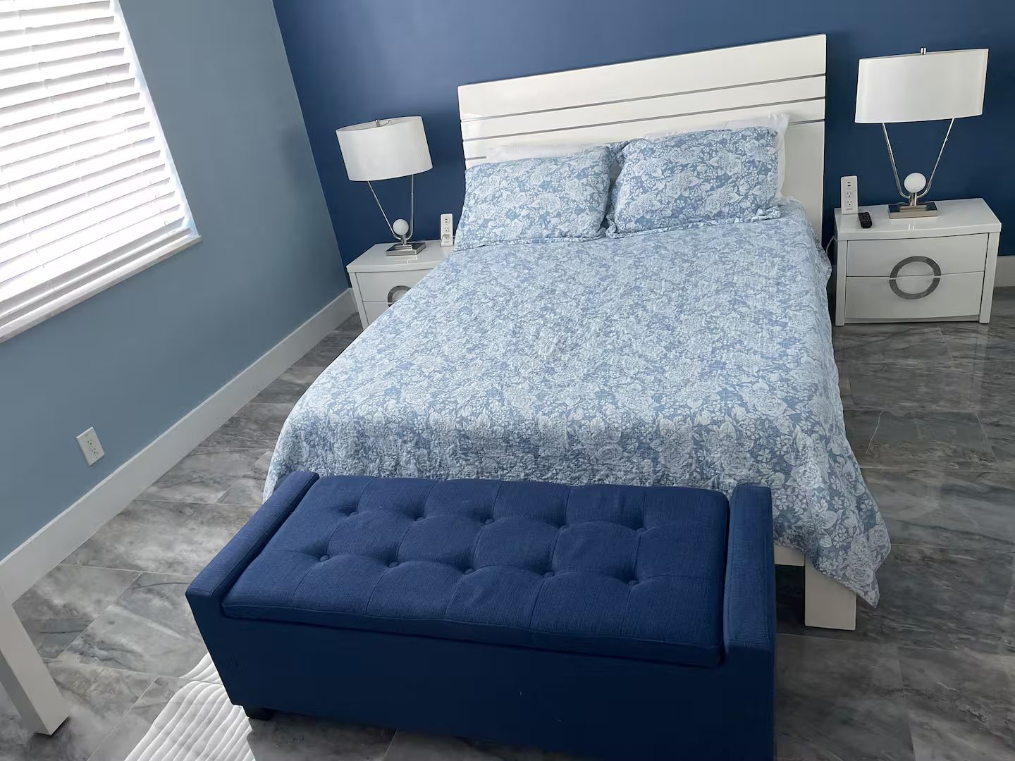 A bedroom with a bed, two bedside tables, a nightstand, a lamp, and a bench.