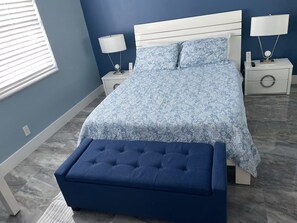 A bedroom with a bed, two bedside tables, a nightstand, a lamp, and a bench.
