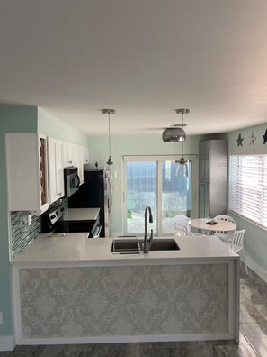 A modern kitchen with a central island, a dining area with a round table, and a view through a glass door.