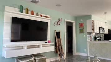 A living room with a flat-screen TV, a painting, and a guitar leaning against the wall.