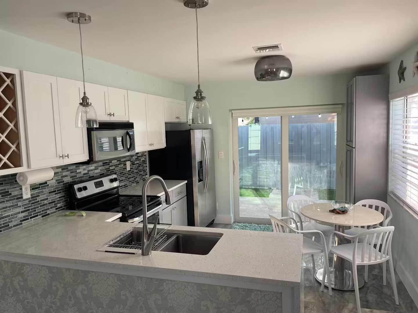 A modern kitchen with a central island, stainless steel appliances, and a dining area with white chairs.