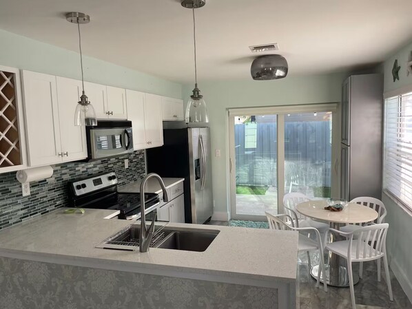 A modern kitchen with a central island, stainless steel appliances, and a dining area with white chairs.