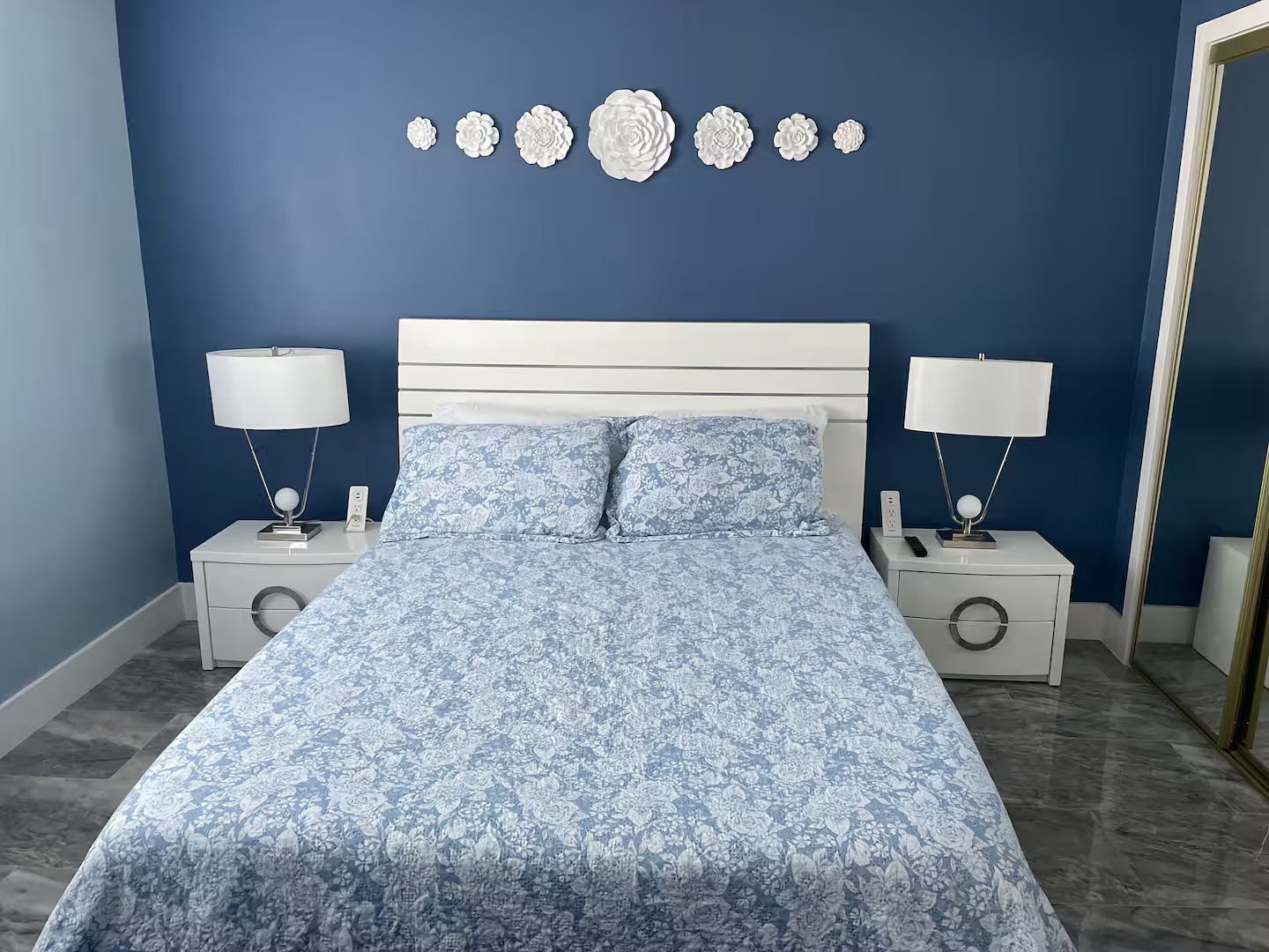 A bedroom with a bed, two bedside tables, two lamps, and a wall decoration.