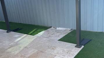 A covered patio area with artificial grass and stone tiles.