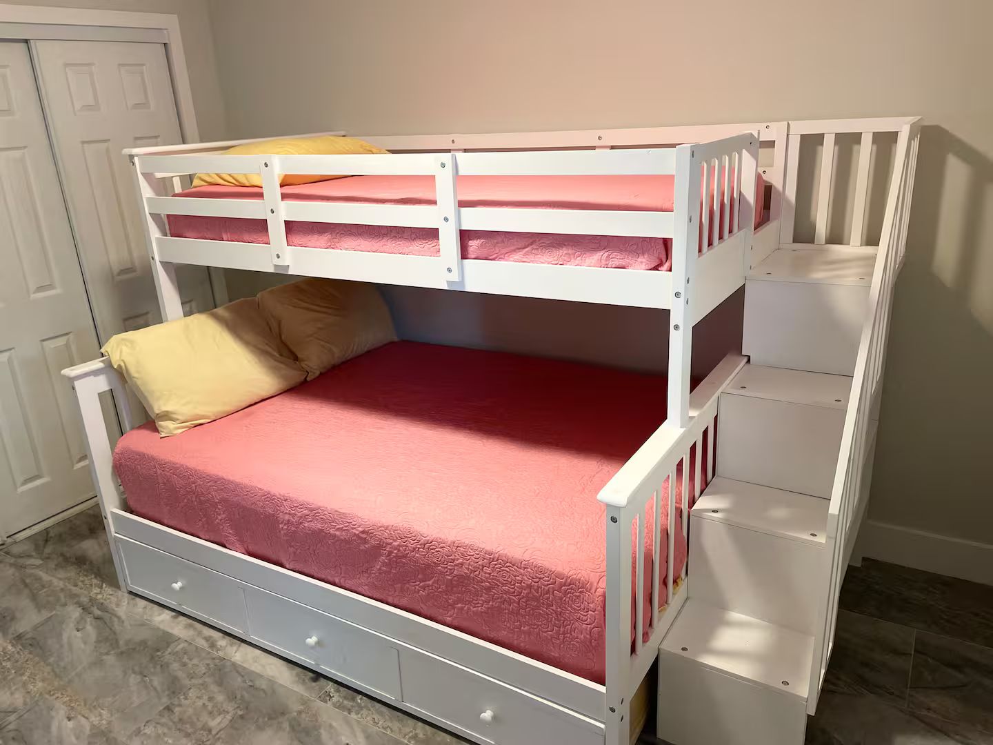 Una cama litera con un cajón debajo, una cama individual arriba y una puerta blanca al fondo.