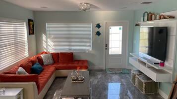 A living room with a sectional sofa, a flat-screen TV, a coffee table, and a door with a frosted glass window.