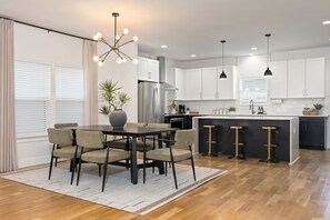 A modern kitchen with white cabinets, a stainless steel refrigerator, a dining area with a table and chairs, and a bar area with stools. - Nashville Dream Home - Near Downtown, Broadway, Midtown and Much More! (Nashville)