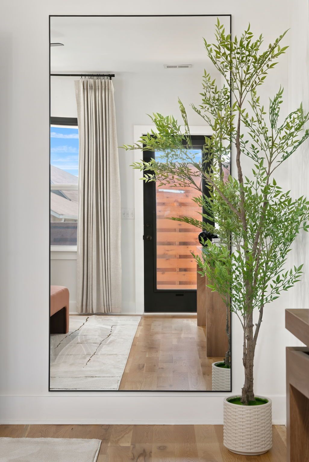 Ein modernes Interieur mit Holzboden, einer Topfpflanze, einer Bank und Blick durch eine Tür in einen Außenbereich mit einer Holzverkleidung und einem Fenster.