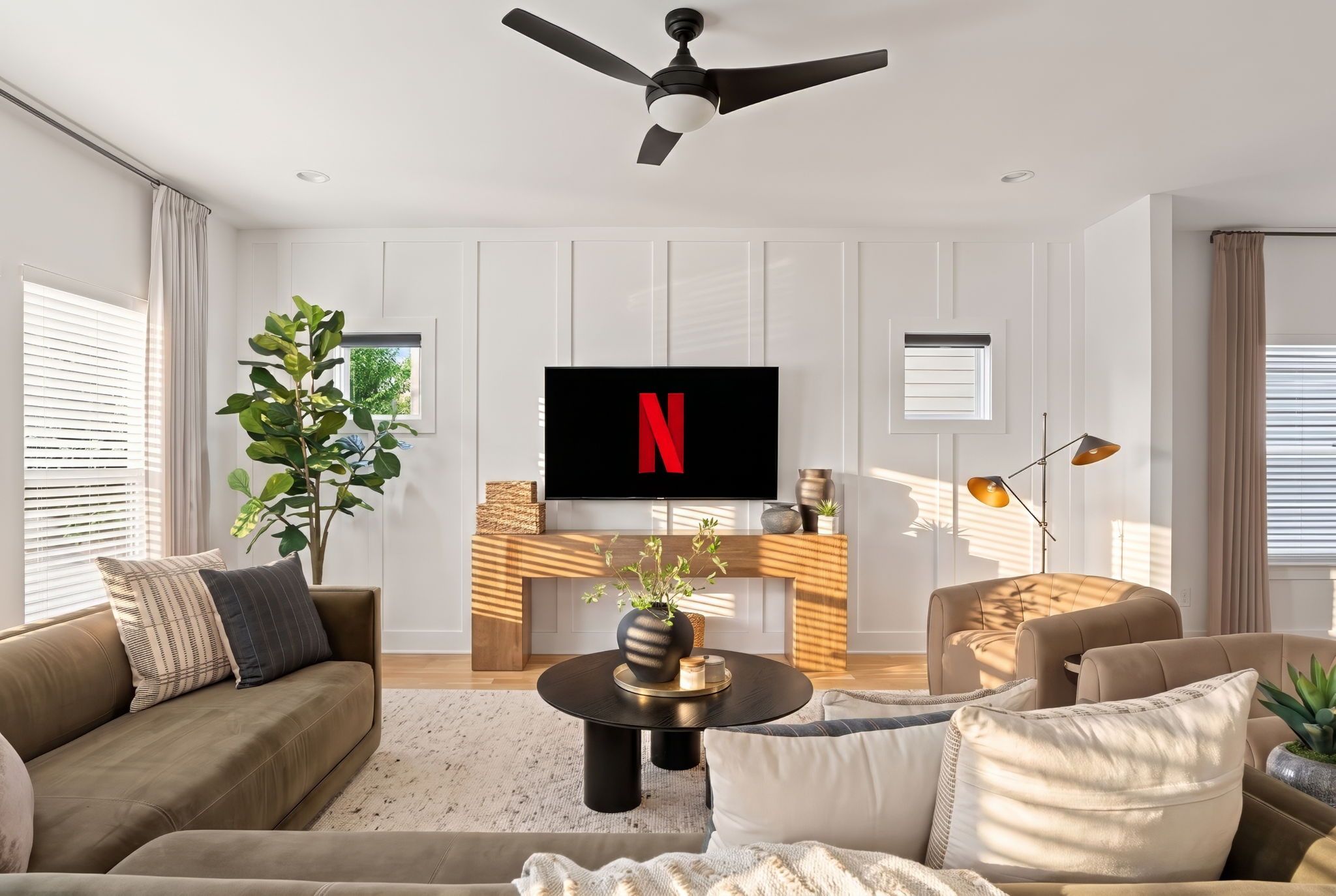 Una sala de estar moderna con un televisor de pantalla plana mostrando el logotipo de Netflix, un ventilador de techo y una chimenea.