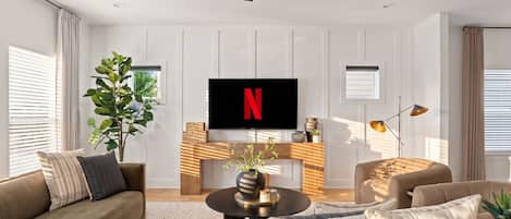 Una sala de estar moderna con un televisor de pantalla plana mostrando el logotipo de Netflix, un ventilador de techo y una chimenea.