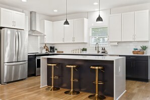 A modern kitchen with white cabinetry, a stainless steel refrigerator, a central island with bar stools, and pendant lighting. - Nashville Dream Home - Near Downtown, Broadway, Midtown and Much More! (Nashville)