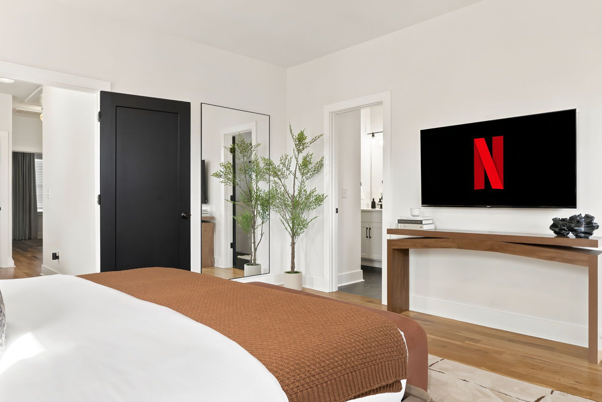 Een hotelkamer met een bed, een aan de muur bevestigde televisie, een plant en een houten nachtkastje.