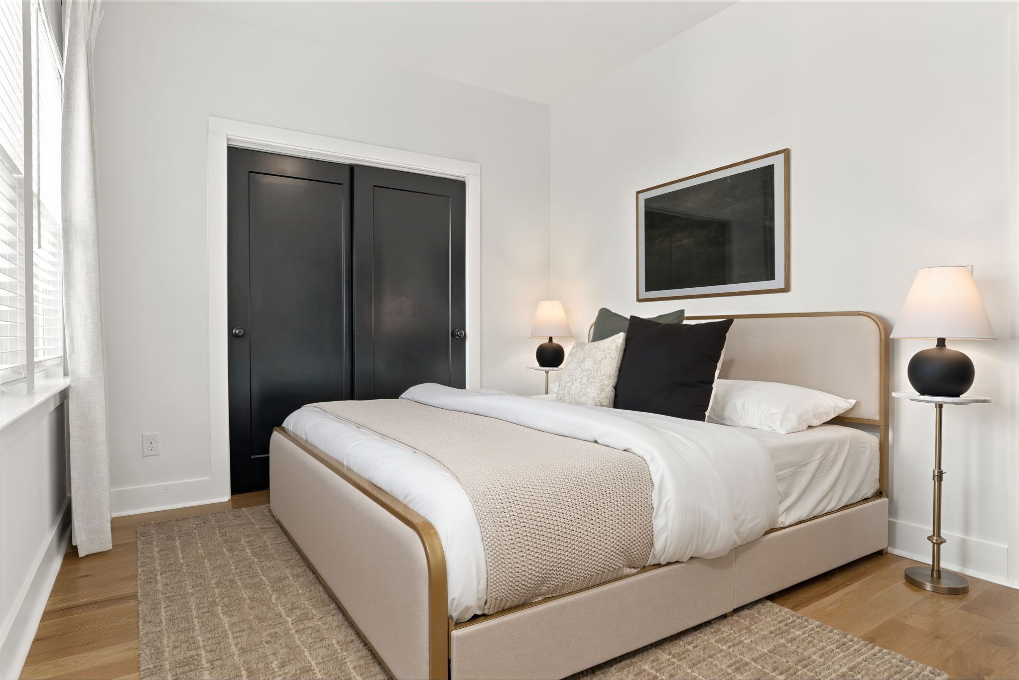 Um quarto com cama, abajures, uma porta e um quadro na parede.
