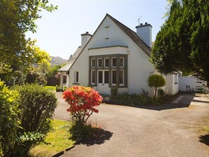 A two-story house with a sloped roof, a chimney, and a small garden with a red flowering plant. - White Gables (Ambleside)