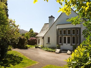 Ein Haus mit befestigter Auffahrt, einem Garten mit verschiedenen Pflanzen und blauem Himmel.