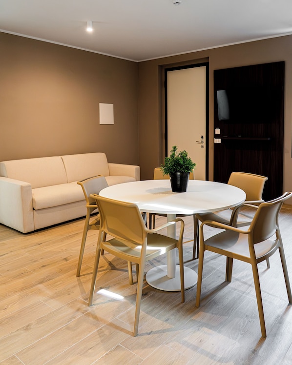 A modern living room with a round dining table, four chairs, a sofa, and a potted plant.