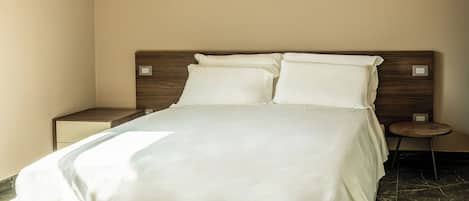 Quarto de hotel com uma cama grande, cabeceira de madeira, mesa de cabeceira e uma pequena mesa redonda.