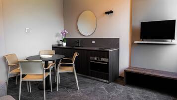 Eine moderne Küche mit einem runden Esstisch, Stühlen, einer kleinen Topf-Orchidee und einem flachbildfernseher an der Wand.