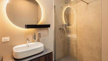 Ein modernes Badezimmer mit einer ein Glasfach raumseitig geschlossenen Dusche, einem weißen Waschbecken und einem wandmontierten Spiegel mit runder Beleuchtung.
